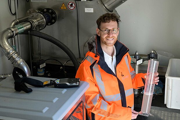 Ein Mann mit einer Wasserprobe in der Hand in einem technischen Umfeld.