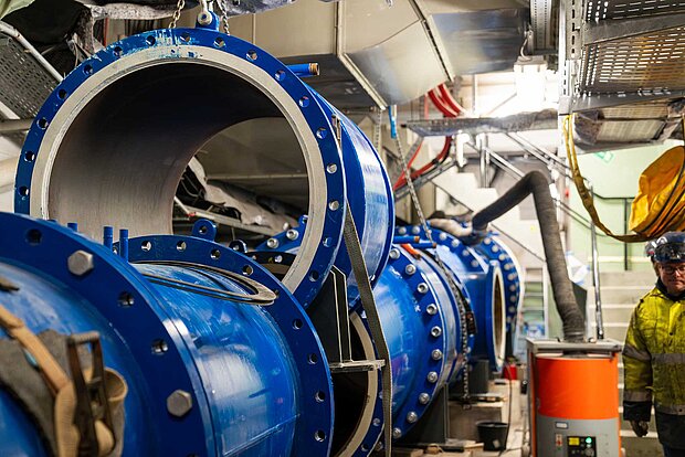 Blaue Rohre werden in einem kellerartigen Raum unter dem Pumpwerk von Handwerkern eingebracht.