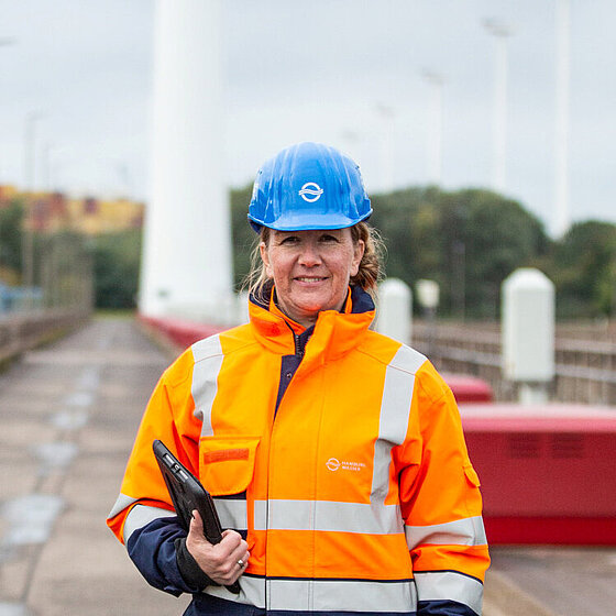 Ingenieurin Daniela mit Signaljacke und Helm. Unter dem Arm trägt sie ihr Tablet.