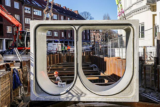 Ein Rohrsegment wird mit einem Kran in die Baugrube eingesetzt.