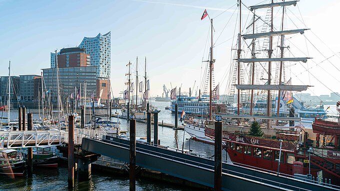 Blick über den Hamburger Hafen. Im Vordergrund liegen Schiffe, im Hintergrund ist die Elbphilharmonie zu sehen.