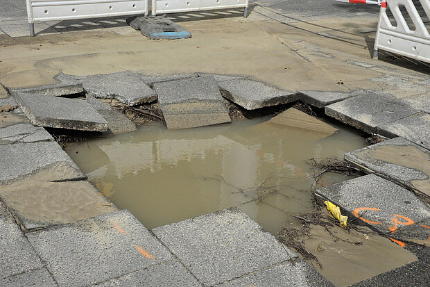 Wasser steht unter den Platten eines Bürgersteigs.