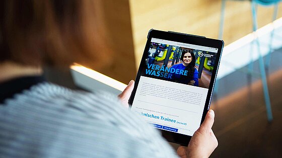Eine Frau schaut sich die HAMBURG WASSER Website auf einem Tablet an.