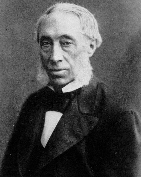 Eine Schwarz-Weiß-Fotogragie, die einen älterer Herr mit weißem Backenbart zeigt.