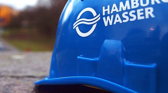 SYMBOLFOTO Blauer HAMBURG WASSER Helm vor unscharfem Hintergrund.