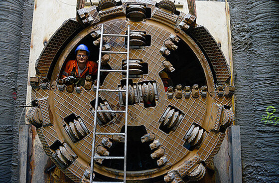 Ein Bohrkopf, mit dem Leitungen tief unter der Erde verlegt werden. Damit die Dimensionen klar werden, ist ein Mitarbeitender in das technische Gerät gestiegen, der Bohrkopf ist rund doppelt so hoch wie er.