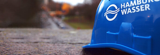 SYMBOLFOTO Blauer HAMBURG WASSER Helm vor unscharfem Hintergrund.