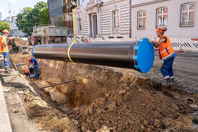 Eine neue Wasserleitung hängt an einer Baggerschaufel und wird in die Baugrube eingebracht.